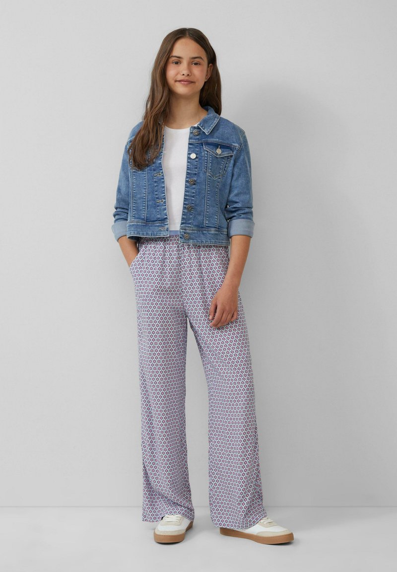 Denim jack, lichtblauw, cropped stijl met knoopsluiting. Witte t-shirt eronder. Vloeiende, gestreepte broek in het wit, blauw en rood. Casual sneakers.