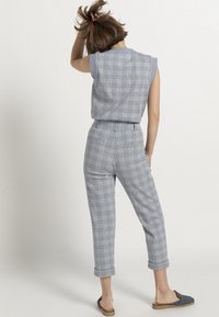 Sleeveless plaid jumpsuit in light blue and gray with a tailored fit. Features a belt, cropped pants, and two back pockets.