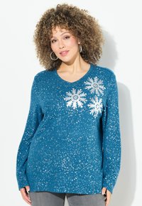 Il maglione lavorato a maglia di colore teal presenta un neckline a V, maniche lunghe, decorazioni in argento a forma di fiocco di neve e un design a macchie in tutto il capo.