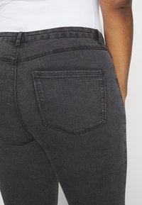 Jeans de mezclilla negra con una textura suave y un bolsillo trasero estándar, que presentan una cintura de altura media y una silueta ajustada.