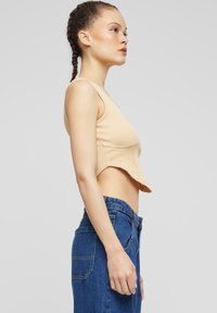 Top corto acanalado beige con tirantes finos, que presenta un diseño ajustado y un dobladillo curvado. Combinado con jeans de mezclilla azul de cintura alta.