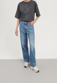 Černé oversize tričko s grafickým potiskem slunce; světlé modré džíny s vysokým pasem; volný střih; nošeno s světle šedými teniskami.