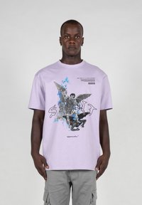 Lilla kortærmet t-shirt med et grafisk print, der viser en figur med vinger og en dæmonisk enhed, med blå accenter og fed tekst.