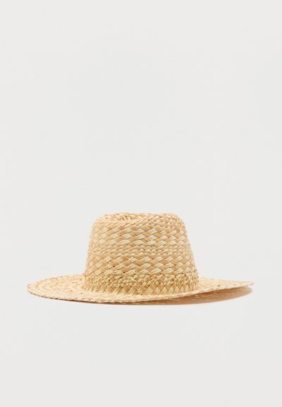 Καπέλο με ευρύ γείσο από άχυρο με υφαντό μοτίβο, φυσικό μπεζ χρώμα, τοποθετημένο σε λευκό φόντο.