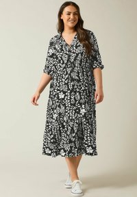 Schwarz-weißer Blumendruckkleid, knielang, mit kurzen Ärmeln und V-Ausschnitt. Verfügt über einen gestuften Rock und wird mit weißen Sneakers getragen.