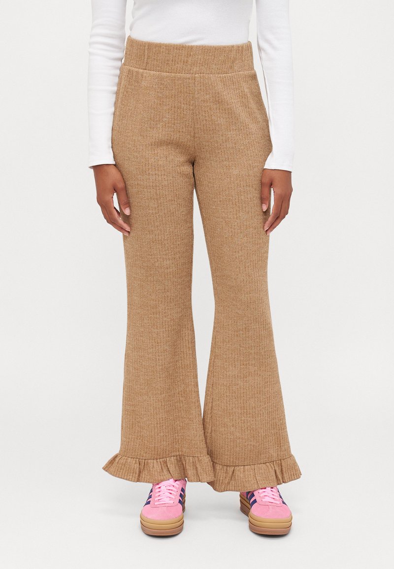 Tan knit flared pants with a ruffled hem and a stretchy waistband, paired with pink sneakers featuring black and navy stripes.