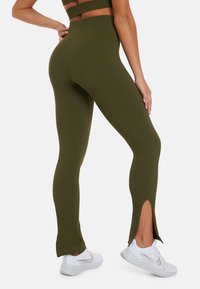 Geribbelde olijfgroene leggings met een hoge tailleband en zijsplitten aan de zoom. Gecombineerd met witte sportschoenen en een bijpassend top.