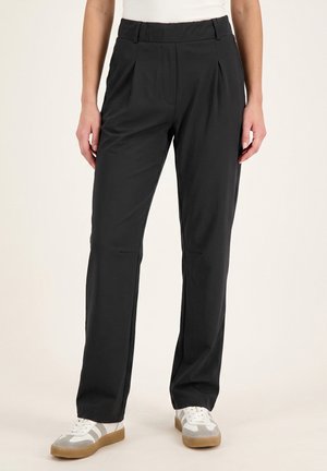 Persoon wearing rechte zwarte broek en witte sneakers met lichtgrijze en beige accenten, staand tegen een effen achtergrond.