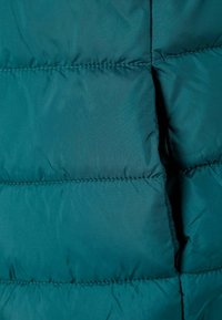 Tirkizna puffer jakna s kvadratnim panelima, glatke teksture, izdržljivog materijala i vidljivim šavovima.