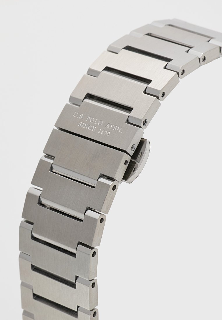 Bracelet de montre en acier inoxydable argenté avec des maillons entrelacés et une finition brossée. Présente le nom de la marque gravé et la date sur le fermoir.