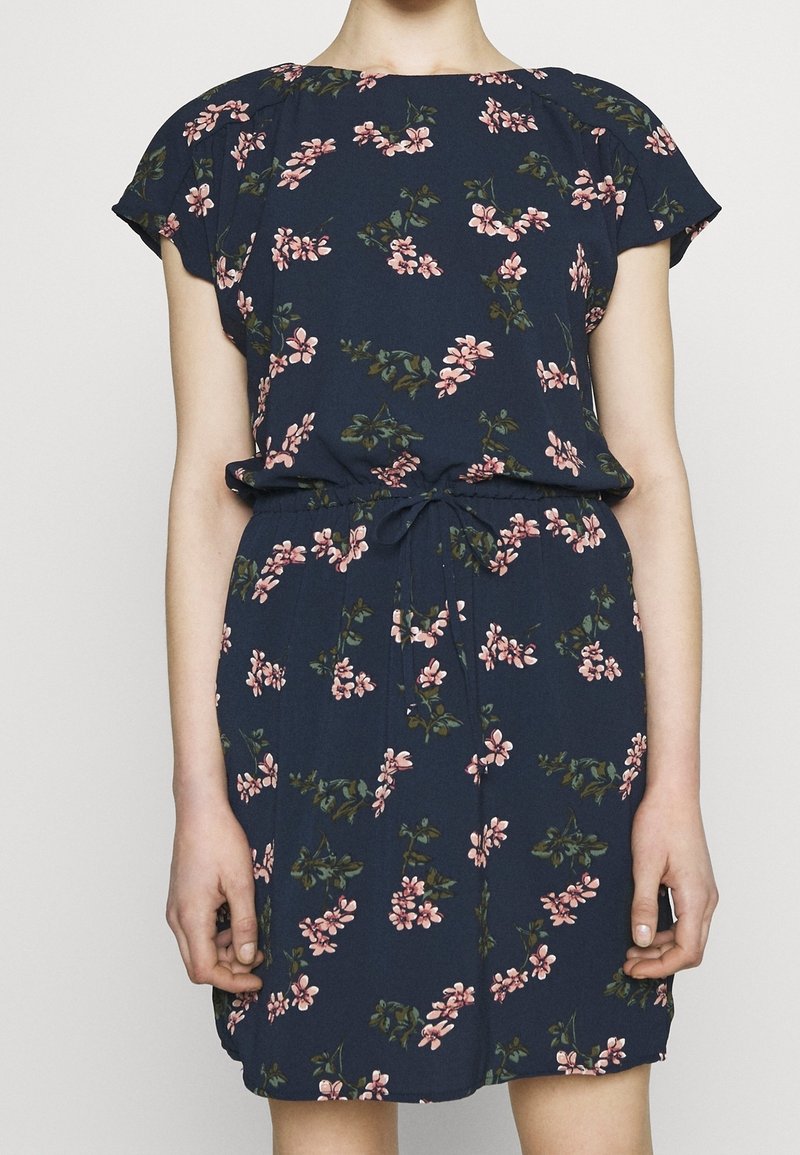 Robe bleu marine avec imprimé floral rose, manches courtes et ceinture à la taille, portée par une personne sur un fond neutre.
