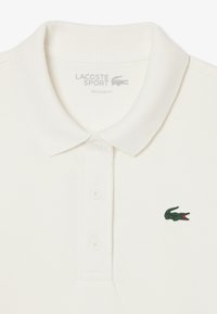 Weißes Polohemd aus strukturiertem Stoff, mit klassischem Kragen, drei Knöpfen und einem grünen gestickten Krokodil-Logo.
