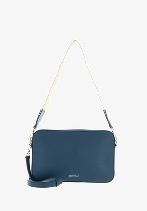 Sac bandoulière rectangulaire en cuir bleu marine avec ferrures dorées, sangle d'épaule beige réglable et nom de la marque "Coccinelle" en lettres dorées.