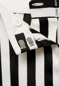 Chemise rayée avec des rayures horizontales noires et blanches, un bouton et deux fermoirs métalliques au col, avec une texture de tissu lisse.