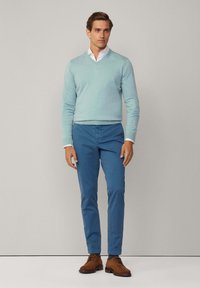 Maglione azzurro chiaro a V, camicia bianca con colletto sotto, chinos blu e scarpe stringate marroni, con una trama liscia e un design aderente.