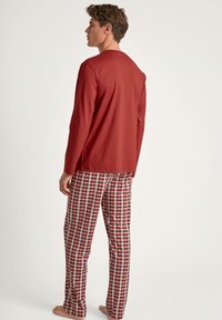 Un haut en coton rouge à manches longues associé à un pantalon de pyjama à carreaux rouge, blanc et noir. La coupe est décontractée avec une taille élastique.