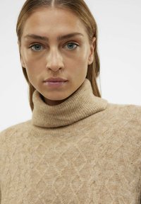 Maglione beige a collo alto in maglia testurizzata con motivo a diamante e colletto a costine, realizzato in un morbido e caldo materiale simile alla lana.
