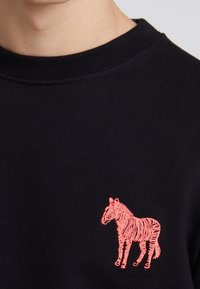 Svart sweatshirt med en rosa broderad zebra-design på vänster bröst. Rund halsringning och ribbad manschett fulländar utseendet.