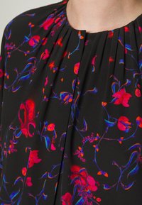 Tissu noir avec des plis et un motif floral vibrant en rouge, rose, violet et bleu autour d'un col rond.