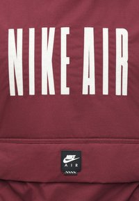 Casaco Nike cor castanha com grandes letras brancas "NIKE AIR". Apresenta um rótulo preto da Nike com detalhes brancos. Textura suave, design simples.