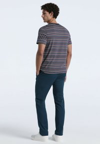 Gestreepte t-shirt met korte mouwen in marineblauw, rood en wit, gecombineerd met donkerblauwe broek en witte sneakers. Achteraanzicht, minimalistisch ontwerp.