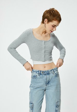 Camiseta corta de punto gris con mangas largas, escote redondeado y botones en la parte delantera. Combinándola con jeans de tiro alto en azul claro que cuentan con bolsillos.