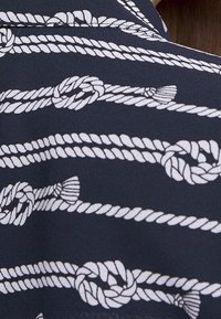 Tessuto blu navy con un motivo di corda bianca, completo di nodi e torsioni. La texture appare liscia, con dettagli chiari e definiti nel design.