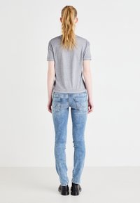 T-shirt gris à manches courtes associé à un jean skinny bleu clair. Le jean a des poches arrière avec des détails de couture subtils et une silhouette ajustée.