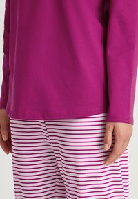 Paars langemouwen top gemaakt van zachte stof, gecombineerd met witte broek met roze horizontale strepen, die een zachte textuur en eenvoudig ontwerp tonen.