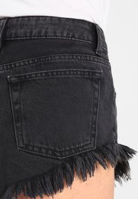 Närbild av svarta jeansshorts med fransade kanter och en bakficka, bärs med en vit topp.