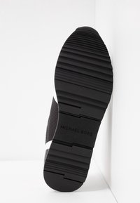 Svart sneakersula med texturerad gummiyta, utrustad med räfflor för grepp och en liten logotyp präglad vid hälen. Ren design och färgkontrast.