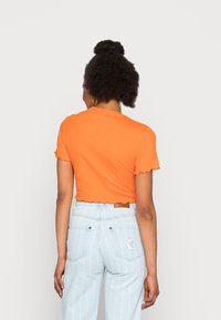 T-shirt cropped laranja com bainha em forma de onda, combinado com jeans de cintura alta com riscas azul claras e um logo na parte de trás.