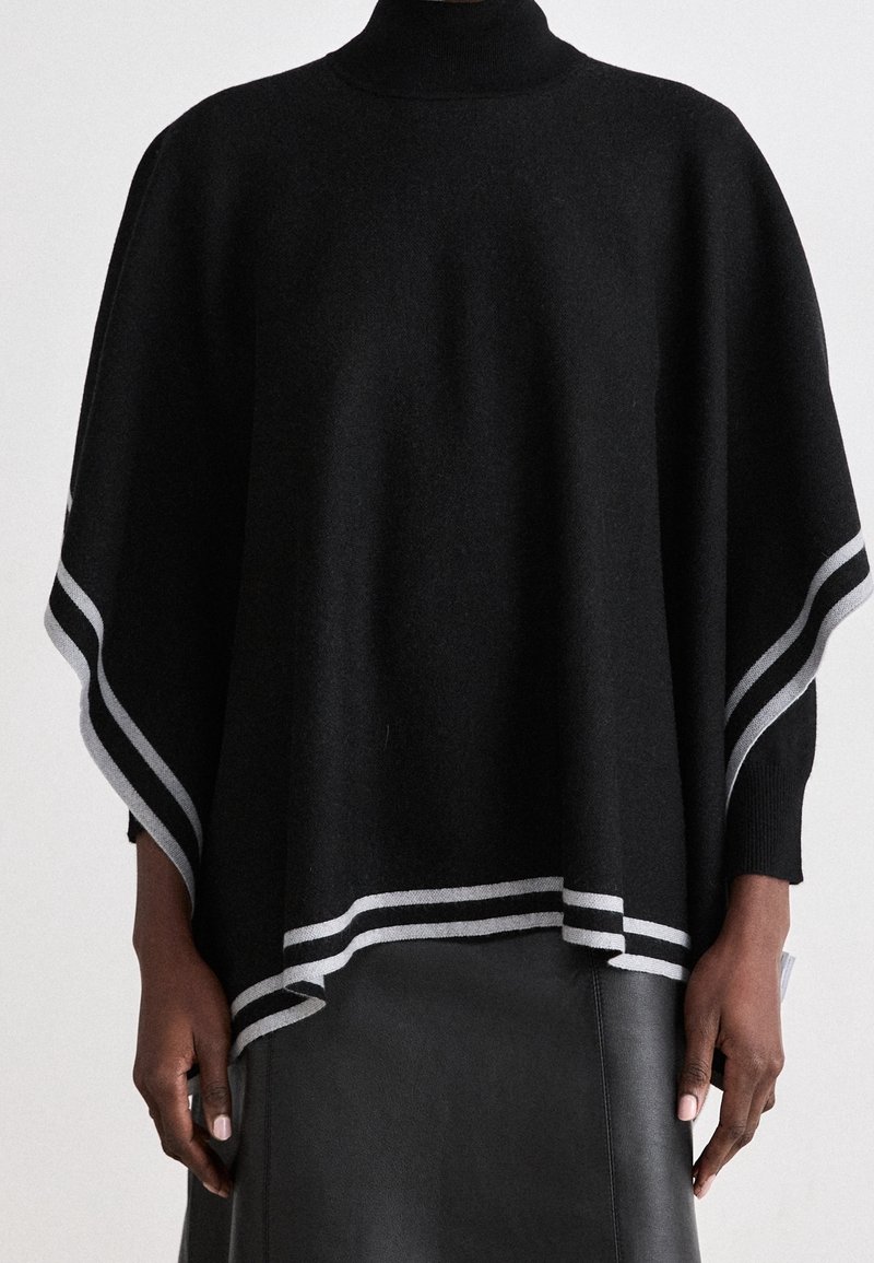Poncho tricoté noir avec un col roulé haut, présentant une bordure rayée grise le long des bords. Texture douce et coupe ample.