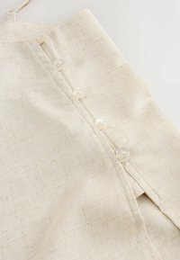 Close-up of beige linen fabric with five small white buttons sewn in a vertical line.