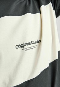 Camiseta de algodón con un diseño de rayas horizontales en negro y crema. El texto en el frente dice "Originals Studio" con detalles de marca debajo.
