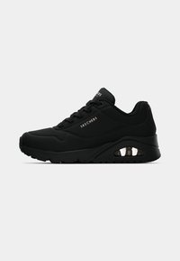 Baskets de sport noires Skechers avec fermeture à lacets à l'avant, semelle rembourrée et coussin d'air visible au talon, logo latéral en lettres blanches.