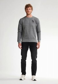 Felpa grigia con polsini e orlo a coste, con un piccolo logo sul petto sinistro; abbinata a jeans neri e sneakers bianche.