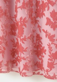 Tessuto rosa trasparente con motivi floreali in velluto corallo, che mostra la trama del tessuto e le pieghe drappeggiate sull'orlo.