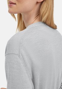 Jasnoszara dzianinowa sweter z luźnym krojem, miękką teksturą i okrągłym dekoltem, z widocznymi szwami na ramionach.