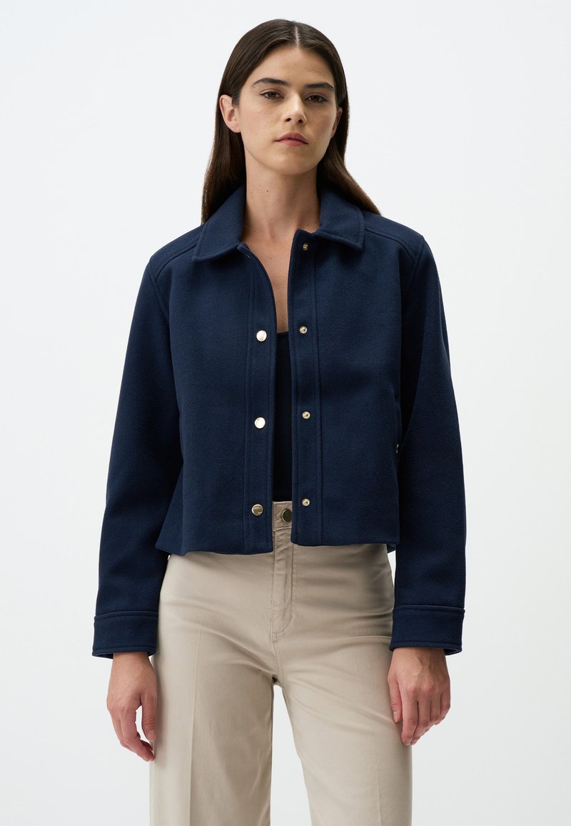 Marineblaue, taillierte Jacke mit Kragen, Knopfleiste und langen Ärmeln. Hergestellt aus einem strukturierten Stoff mit silbernen Hardware-Details.