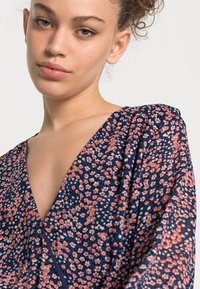 Abito con motivo floreale in blu navy, caratterizzato da piccoli fiori rosa e bianchi. Scollo a V con tessuto morbido e fluido e maniche arricciate.