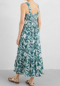Květinové maxi šaty s čtvercovým výstřihem, širokými ramínky a smockovaným zádovým dílem. Obsahují tyrkysové a zelené vzory s vrstvenou sukní.