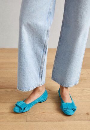 Bailarinas de ante turquesa con punta redondeada, un lazo grande como adorno y tacón bajo, combinadas con vaqueros de pierna ancha en azul claro.