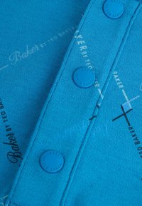 Blau gestrickter Stoff mit zwei passenden Knöpfen; bedruckter Text und grafische Akzente in Weiß und Schwarz; glatte Textur, lässiges Design.
