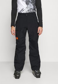 Sorte skibukser med en løs pasform, lynlåsede lommer og et orange logo. Fremstillet af slidstærkt stof, egnet til vintersport.