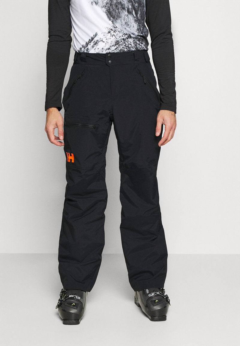 Sorte skibukser med en løs pasform, lynlåsede lommer og et orange logo. Fremstillet af slidstærkt stof, egnet til vintersport.