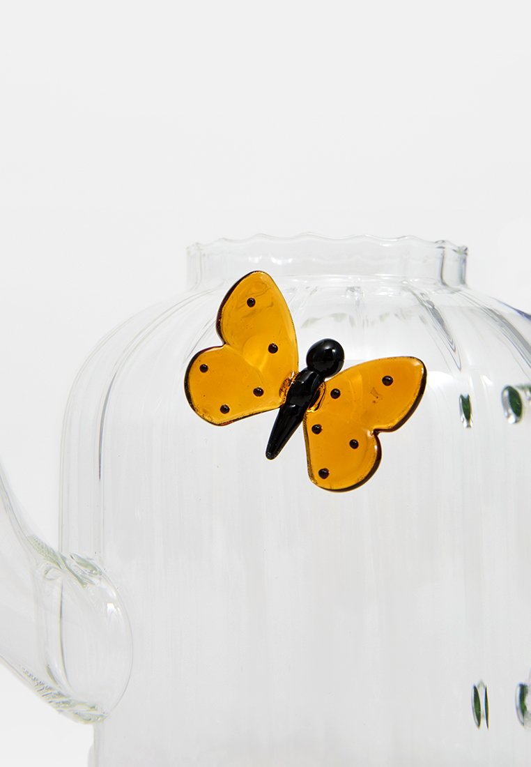 Przezroczysty szklany czajnik z bursztynowym akcentem w kształcie motyla. Czajnik ma żłobioną konstrukcję i zaokrąglony dzióbek do nalewania.