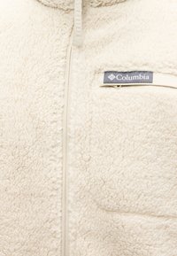 Giacca in pile bianco con chiusura a zip, dotata di una piccola tasca sul petto e una toppa con logo grigio. Texture morbida con un aspetto accogliente.