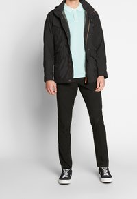 Czarna kurtka z wieloma kieszeniami, jasnoniebieska koszulka polo, czarne spodnie oraz czarne trampki z białymi podeszwami, wykonane z materiałów o teksturowanej powierzchni.