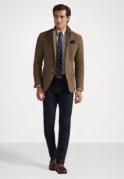 Hnedý houndstooth sako cez svetlú košeľu, vzorovanú kravatu a tmavé džínsy. Hnedé kožené topánky dotvárajú outfit.